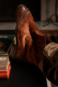 The Legend Boot in rosewood suede, a rich reddish-brown leather boot with a sleek silhouette. Close-up of The Legend Boot in rosewood suede, featuring fine craftsmanship and elegant stitching.