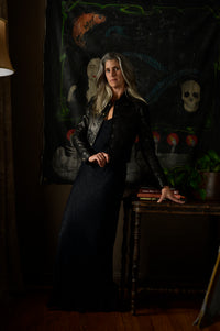 Woman in a dark outfit standing in a dimly lit room with a mystical painting in the background.