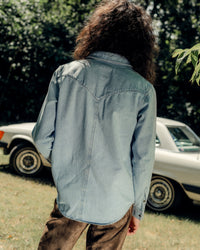 Model wearing The Allen light blue denim shirt in Japanese selvedge cotton, styled with sleeves down and pearl snap front. Posed in front of vintage car.