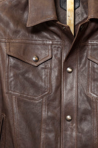 Close-up of a brown leather jacket with buttons and a collar. Softly tailored leather jacket in black lambskin, Savas Denham with structured yet comfortable fit
