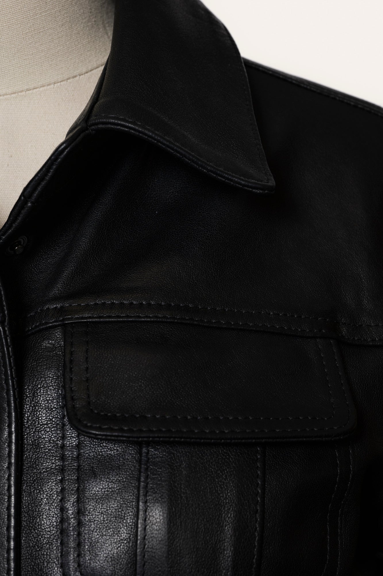 Close-up of a black leather jacket with a pocket detail.