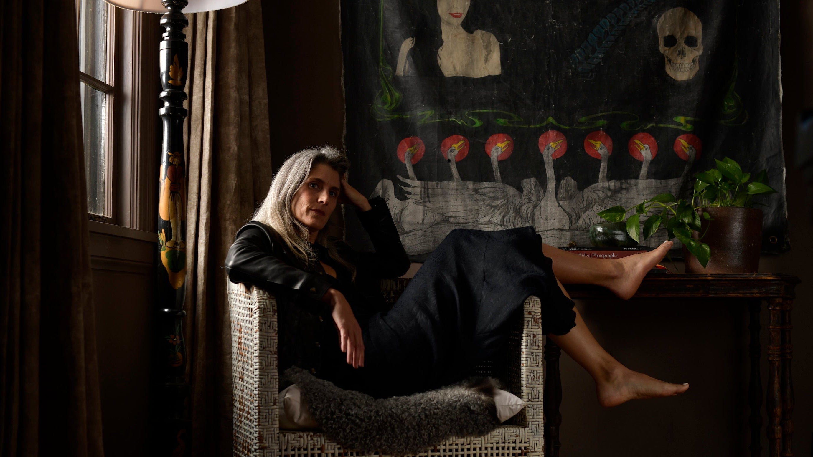 Woman sitting in a chair in a dimly lit room with a painting on the wall.