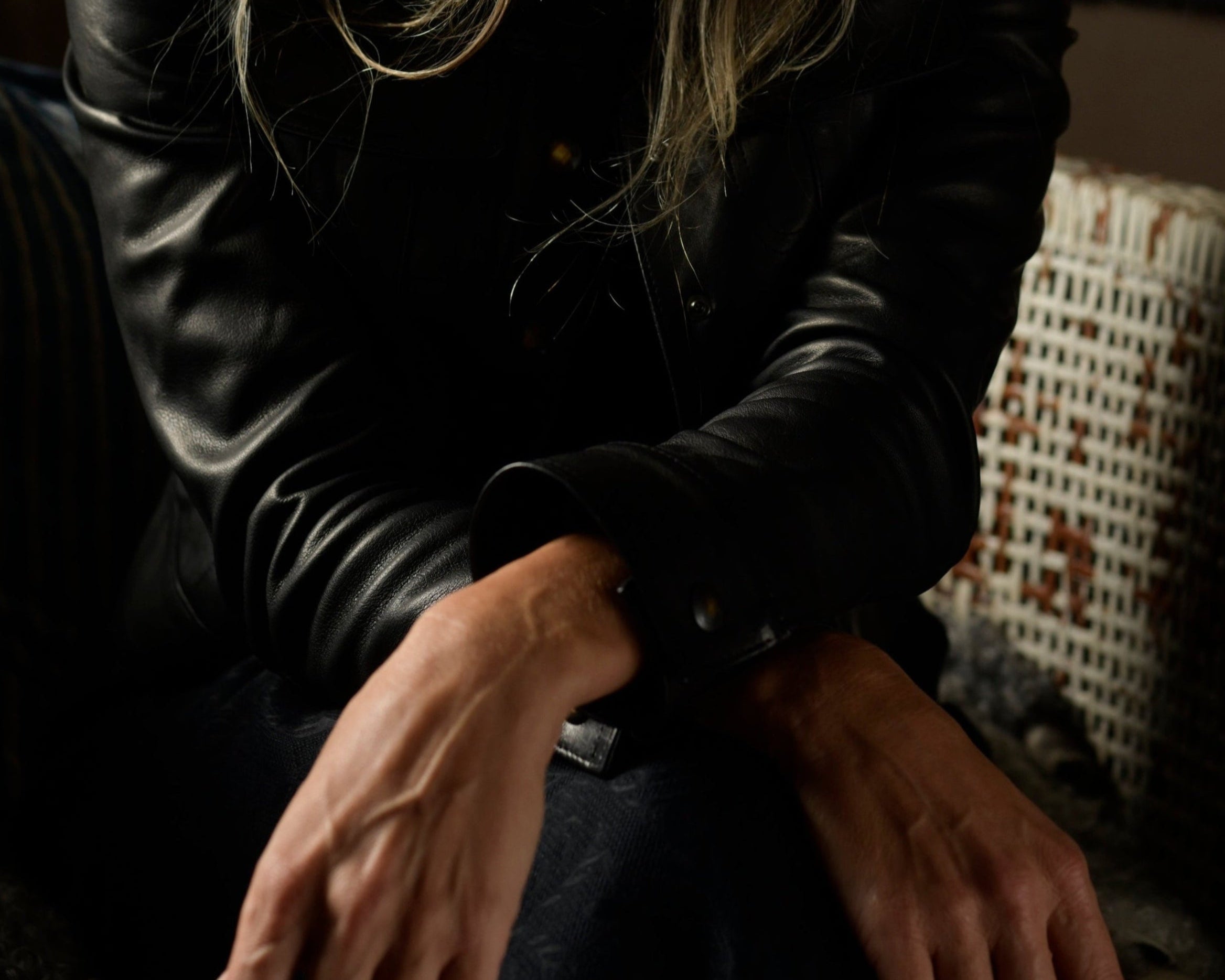 Woman with long gray hair wearing a black leather jacket sitting on a couch.