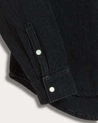 Close-up of black long-sleeve denim shirt cuff with two shell pearl snap buttons