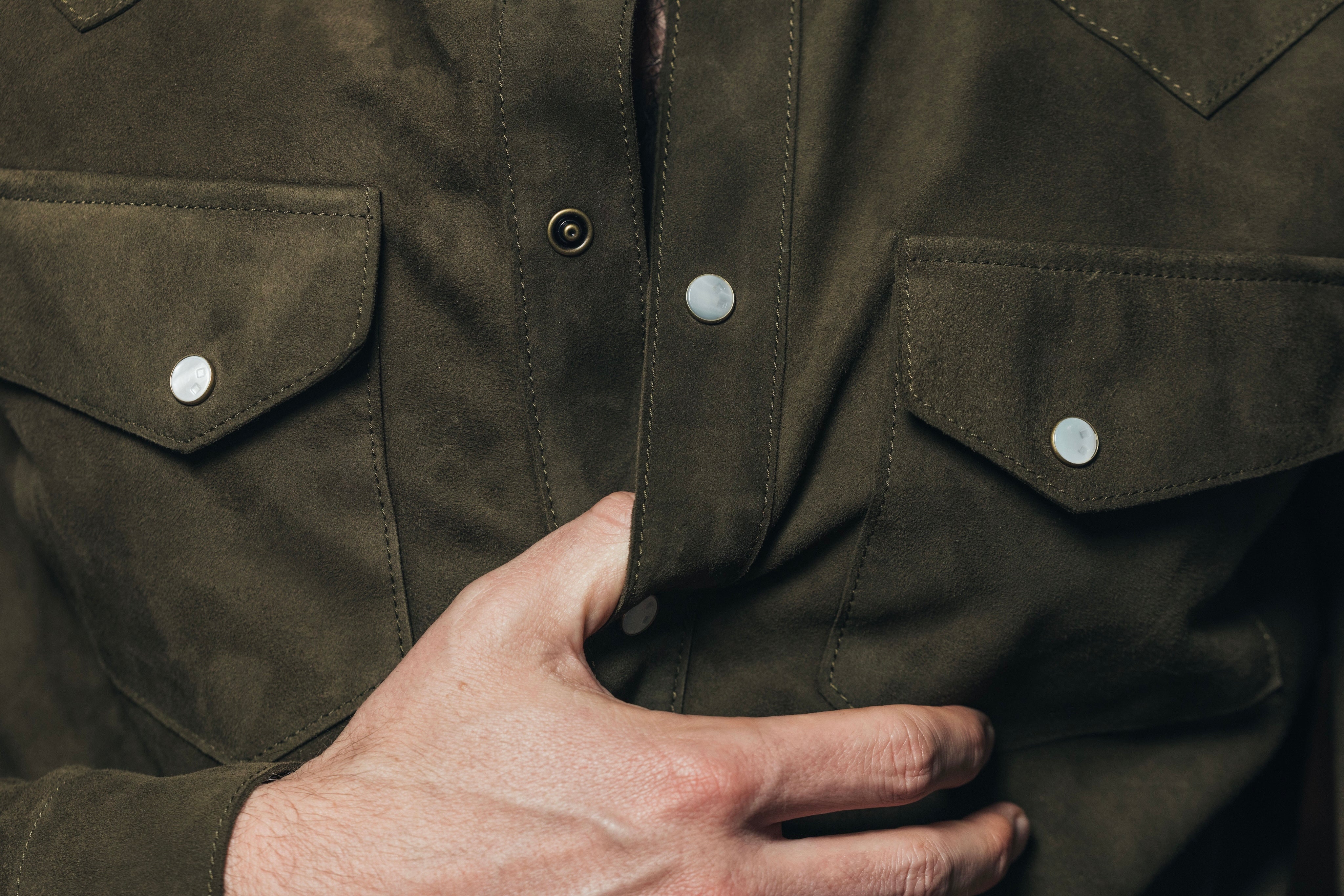 Close-up of a person wearing a dark green jacket with a hand on the chest.