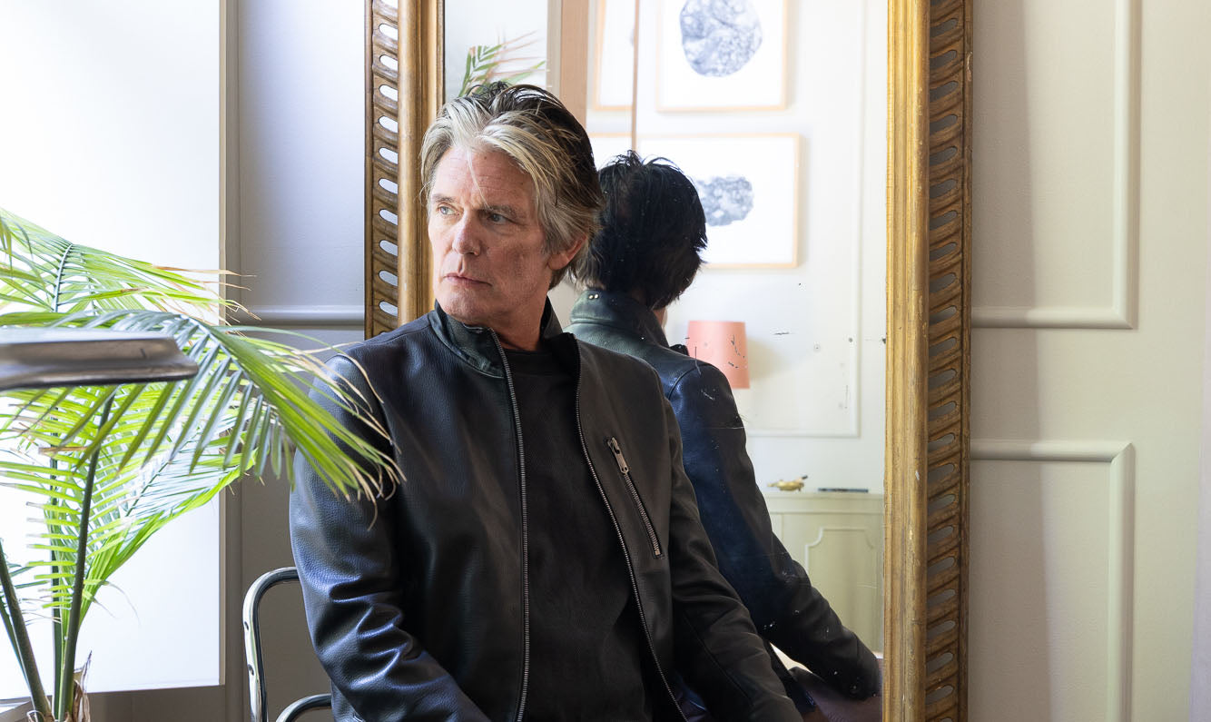 A man with salt and pepper hair sitting in a sunlit room wearing a Savas Jacket