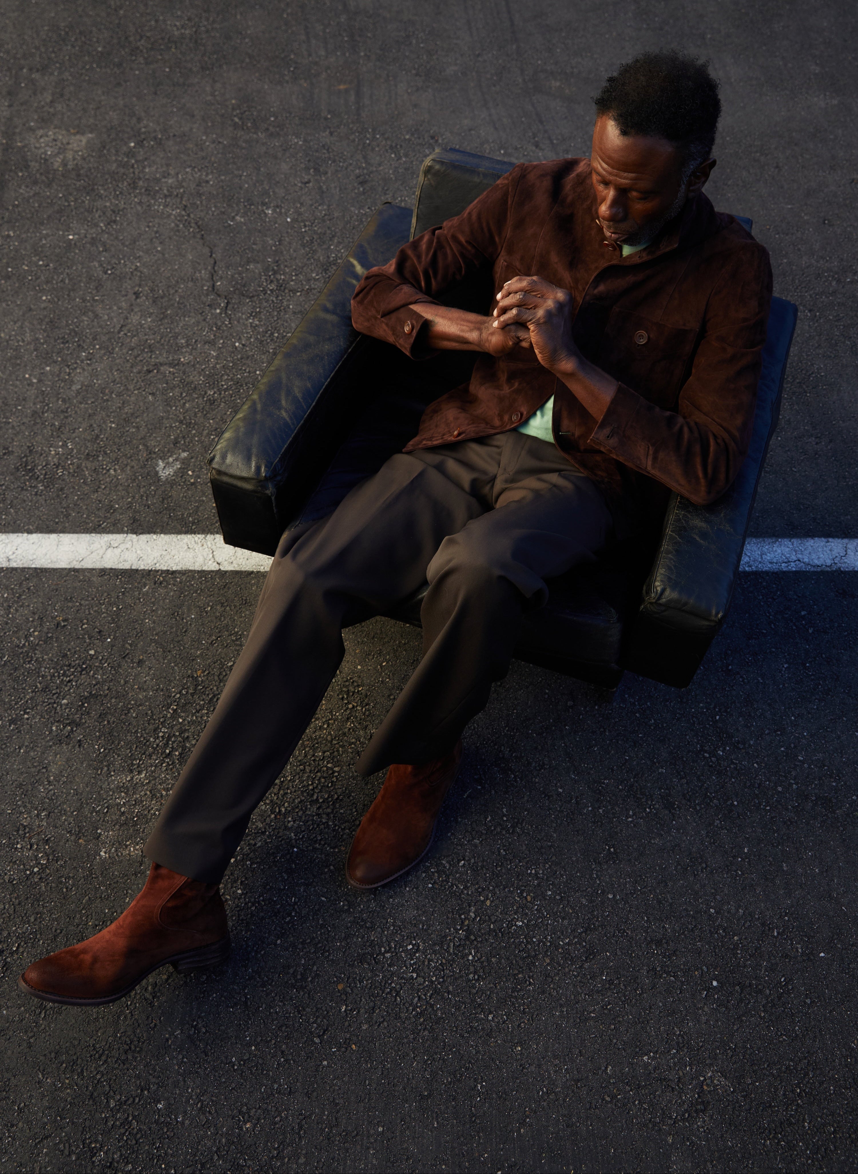 Man sitting on a bench in an urban setting, wearing a brown coat and shoes.
