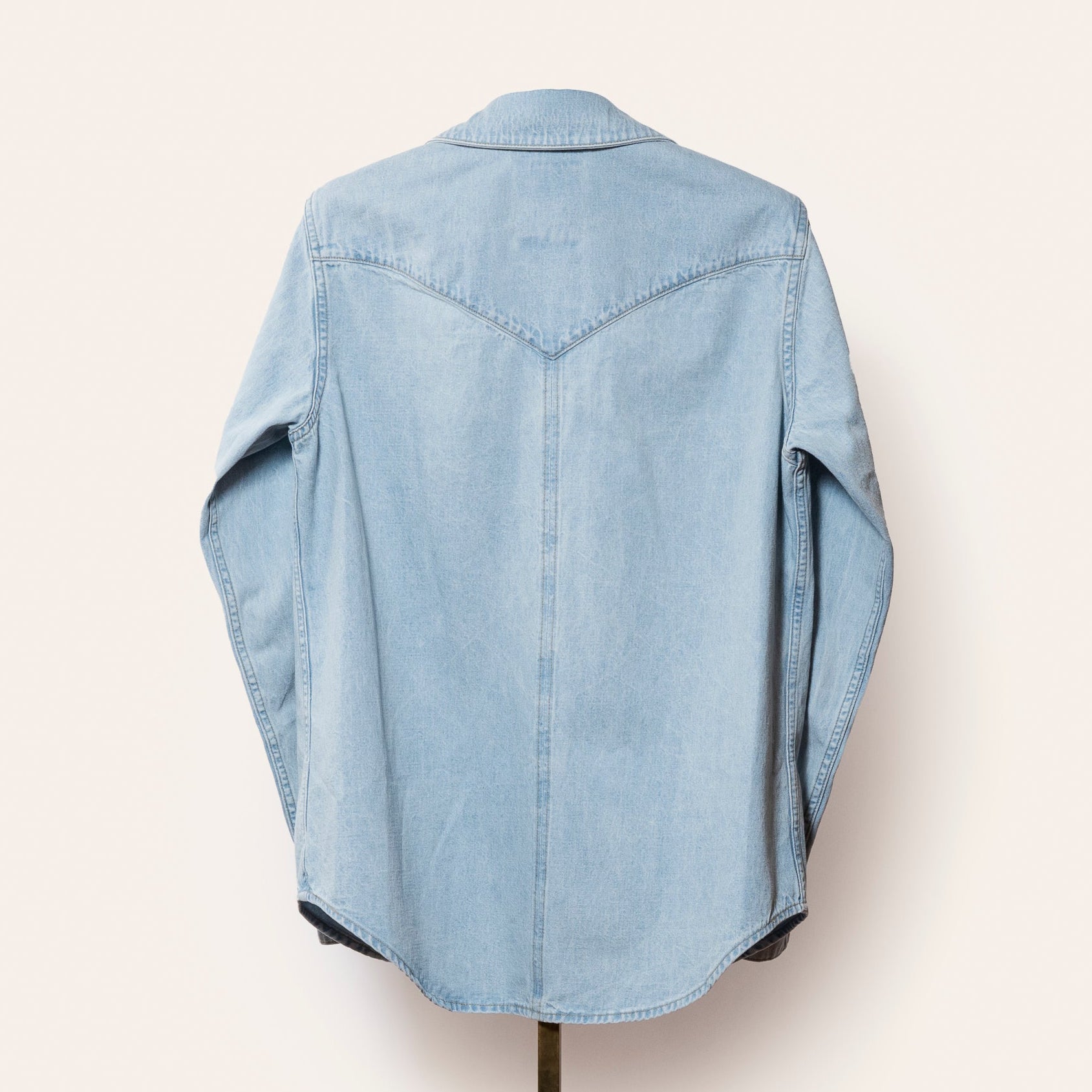 Light blue denim shirt on a hanger against a white background