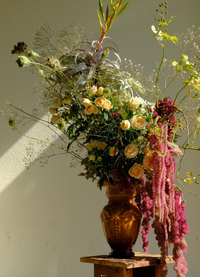 Floral arrangement with a gold vase on a wooden stand against a plain background