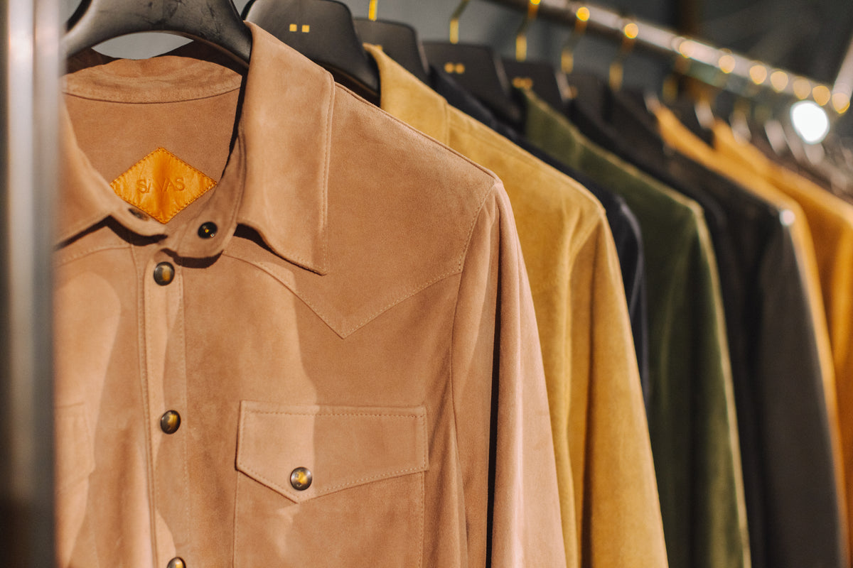 row of suede jackets hanging on a rack with brass coathangers 