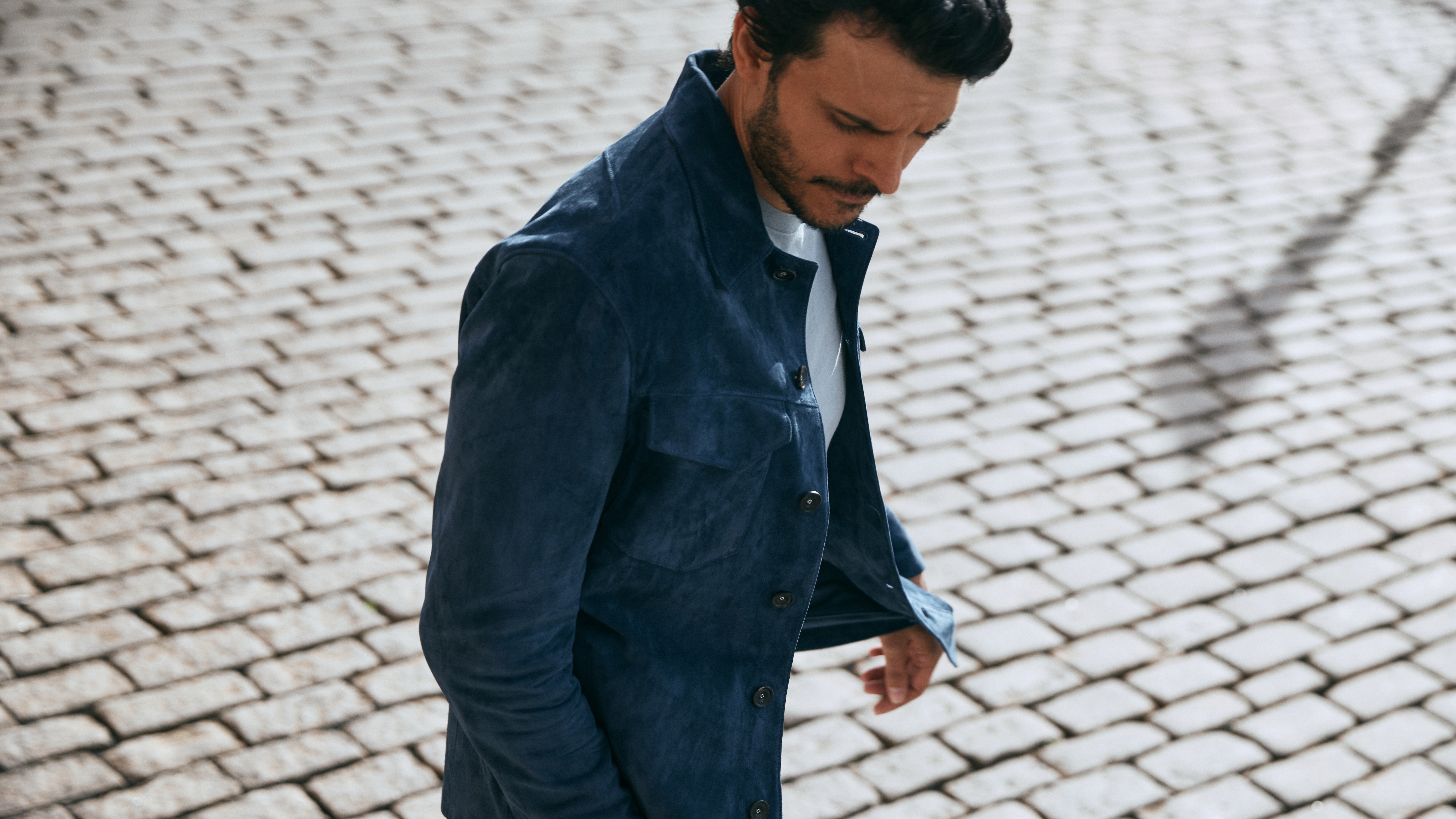 Man in a MARINER BLUE jacket walking on a cobblestone street
