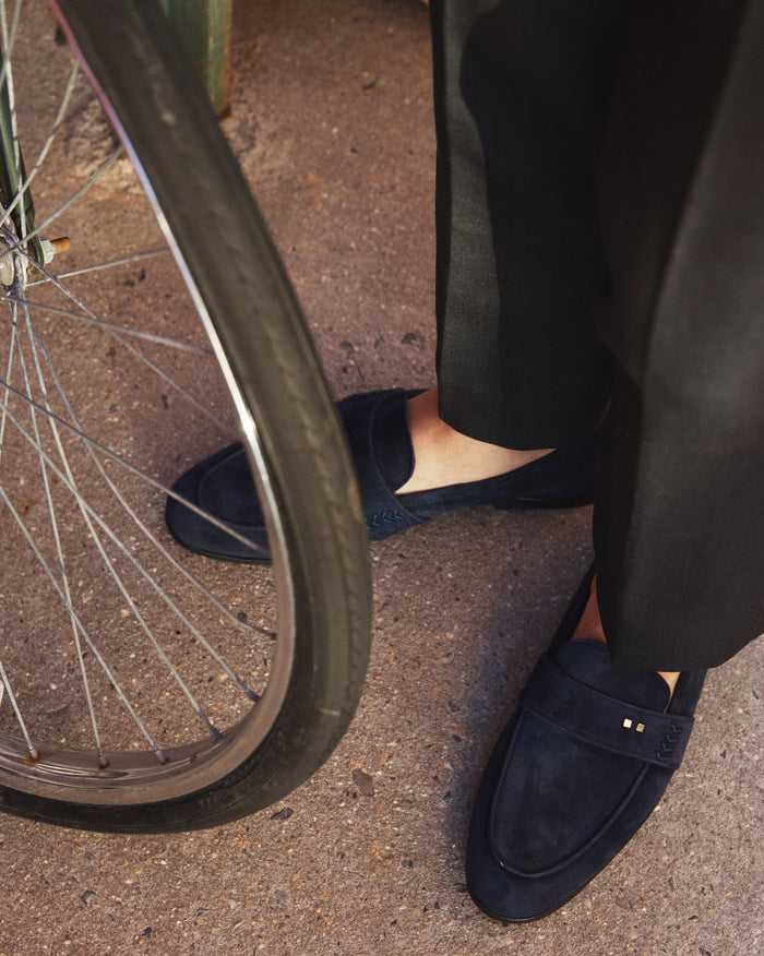 The Coyle sapphire suede loafer worn on-foot in an urban setting, Two Dots brass rivets visible at vamp
