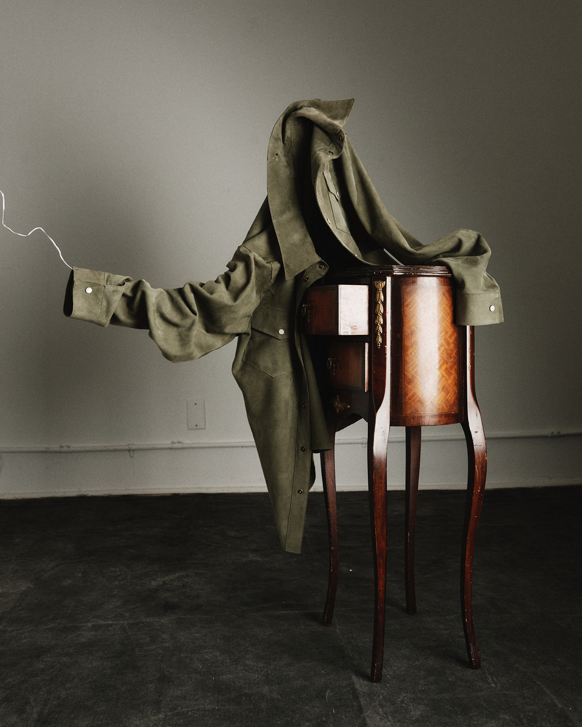 Green coat draped over a wooden stand against a gray wall.