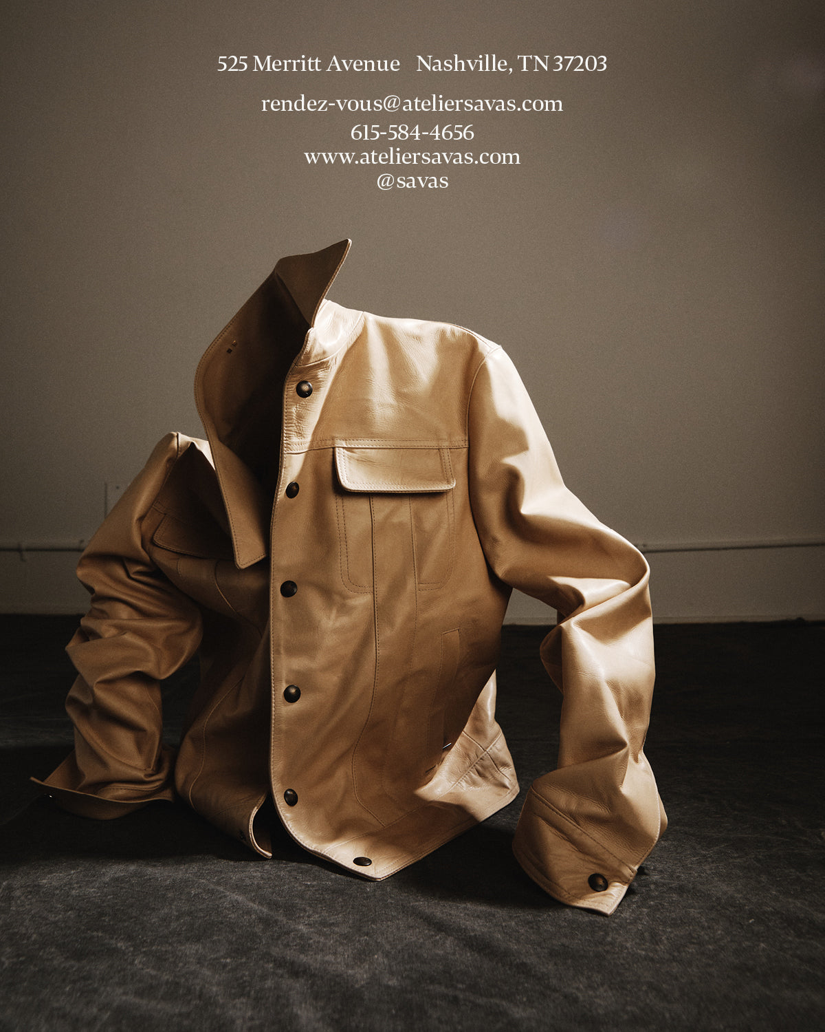 Beige jacket with a hat on a dark surface, with contact information displayed. 525 Merritt Avenue, Nashville, TN 37203 rendez-vous@ateliersavas.com 615-584-4656 www.ateliersavas.com @savas