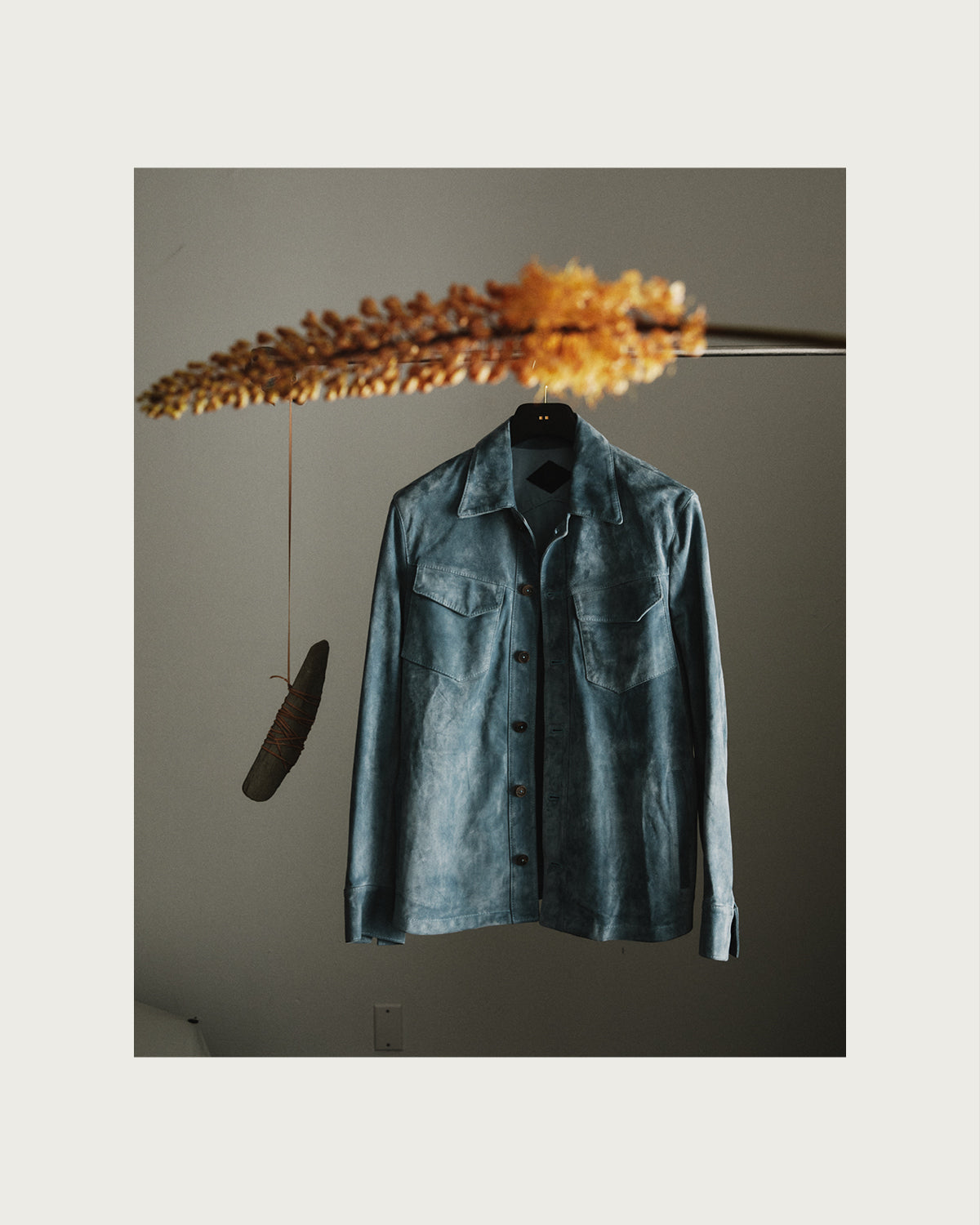 Green denim shirt hanging on a hook against a plain wall with decorative elements.