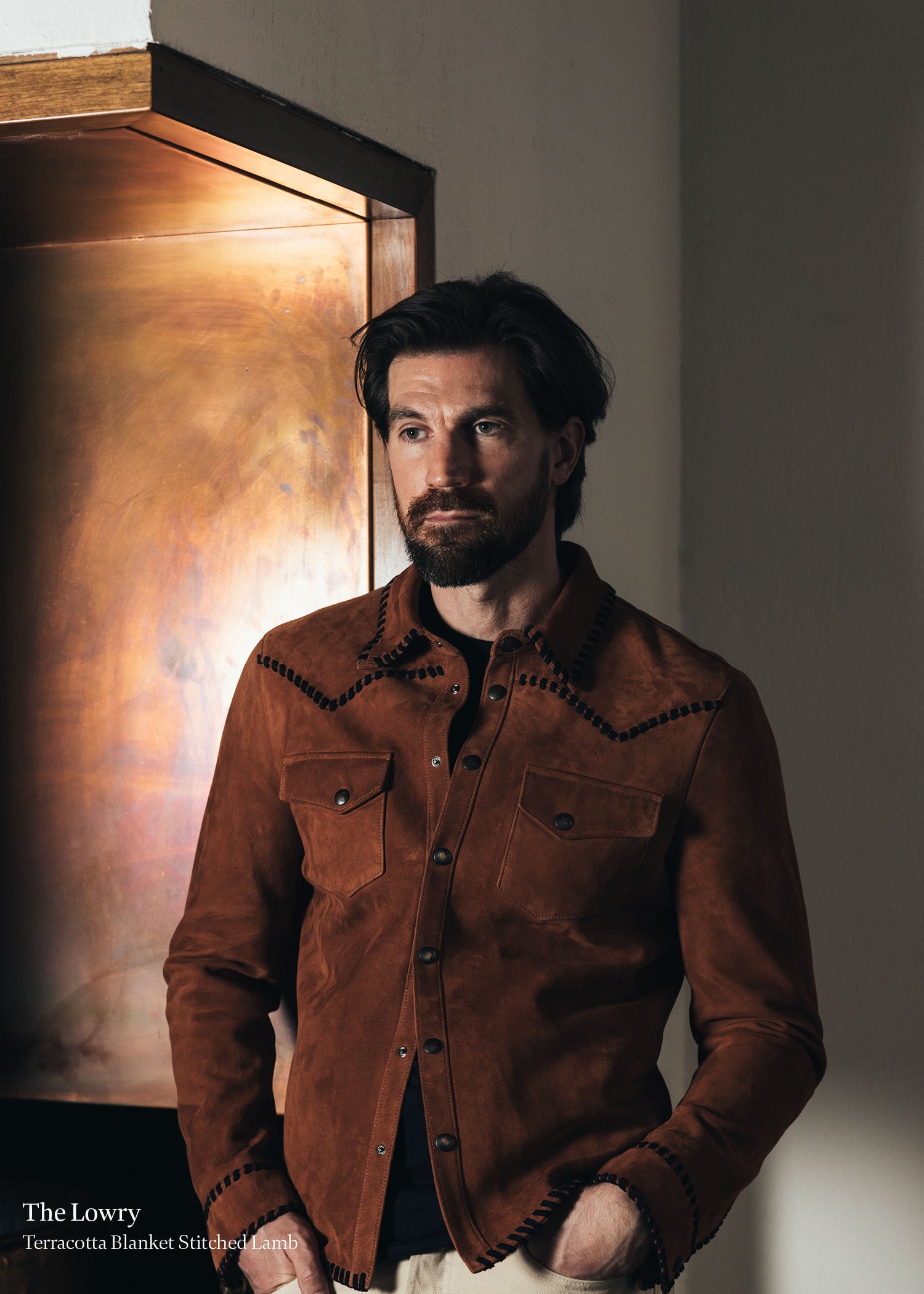 Man wearing a brown jacket standing in front of a textured wall.