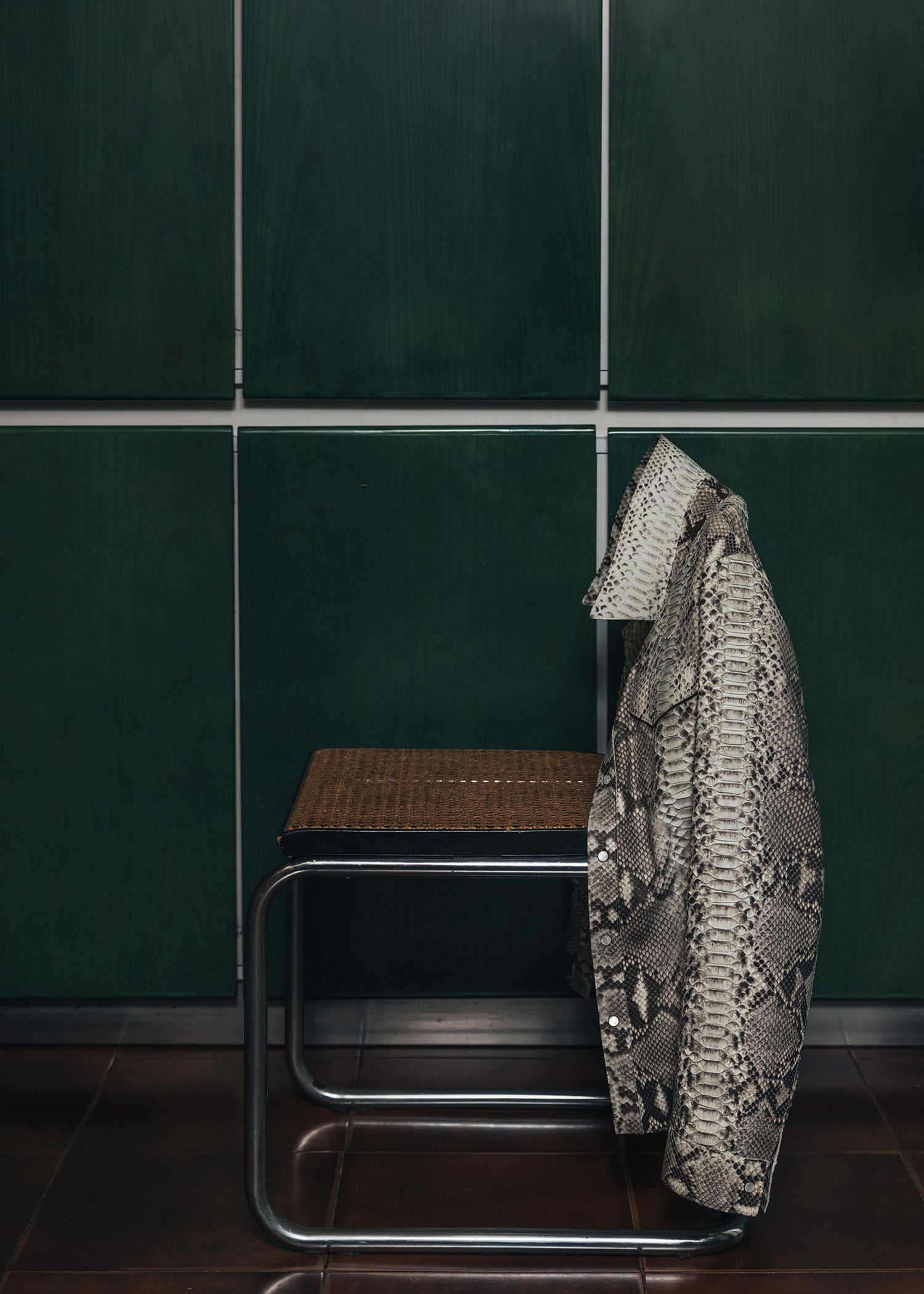Patterned coat hanging on a chair against a green tiled wall.
