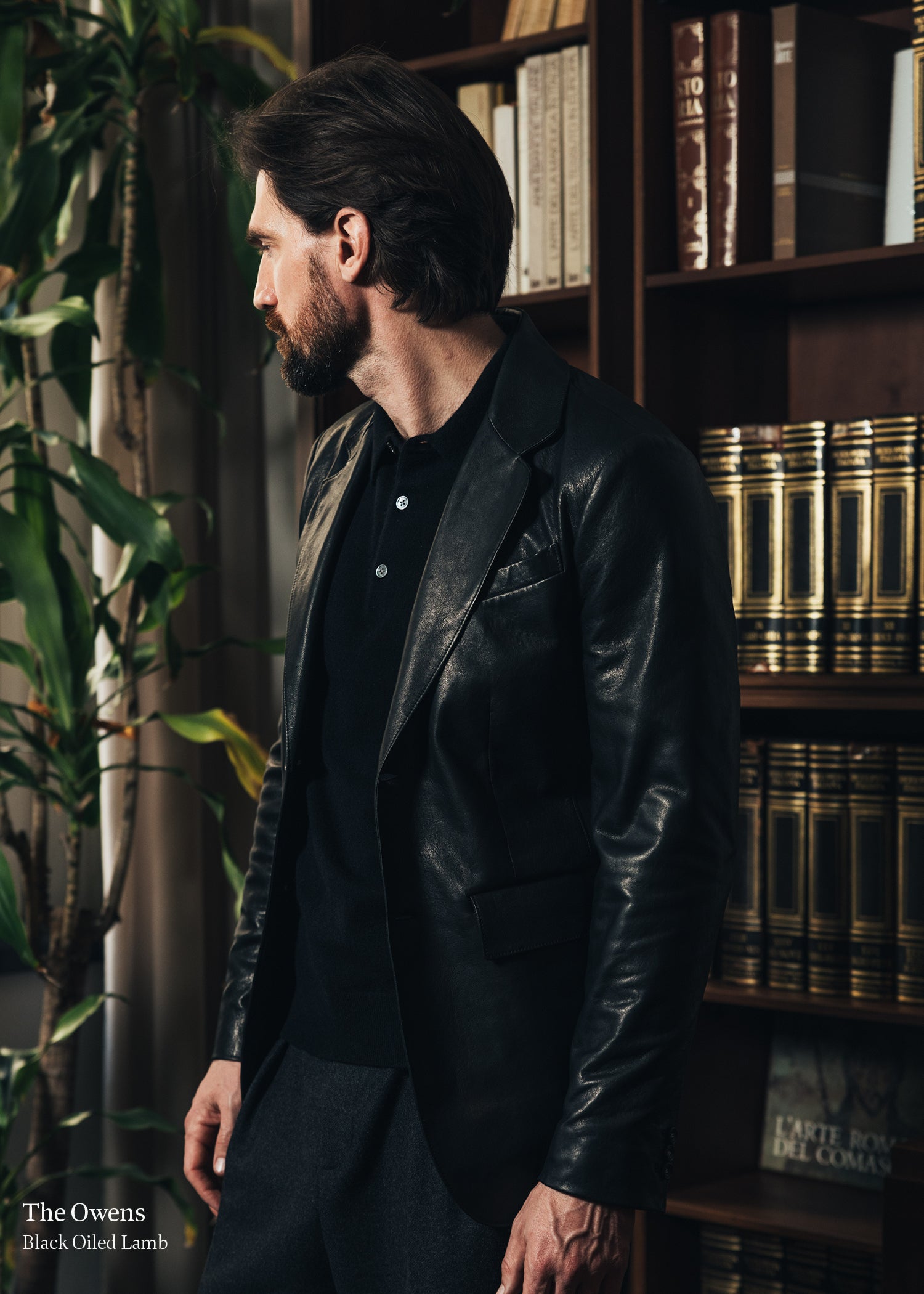 Man in a black leather jacket standing in a room with bookshelves and plants