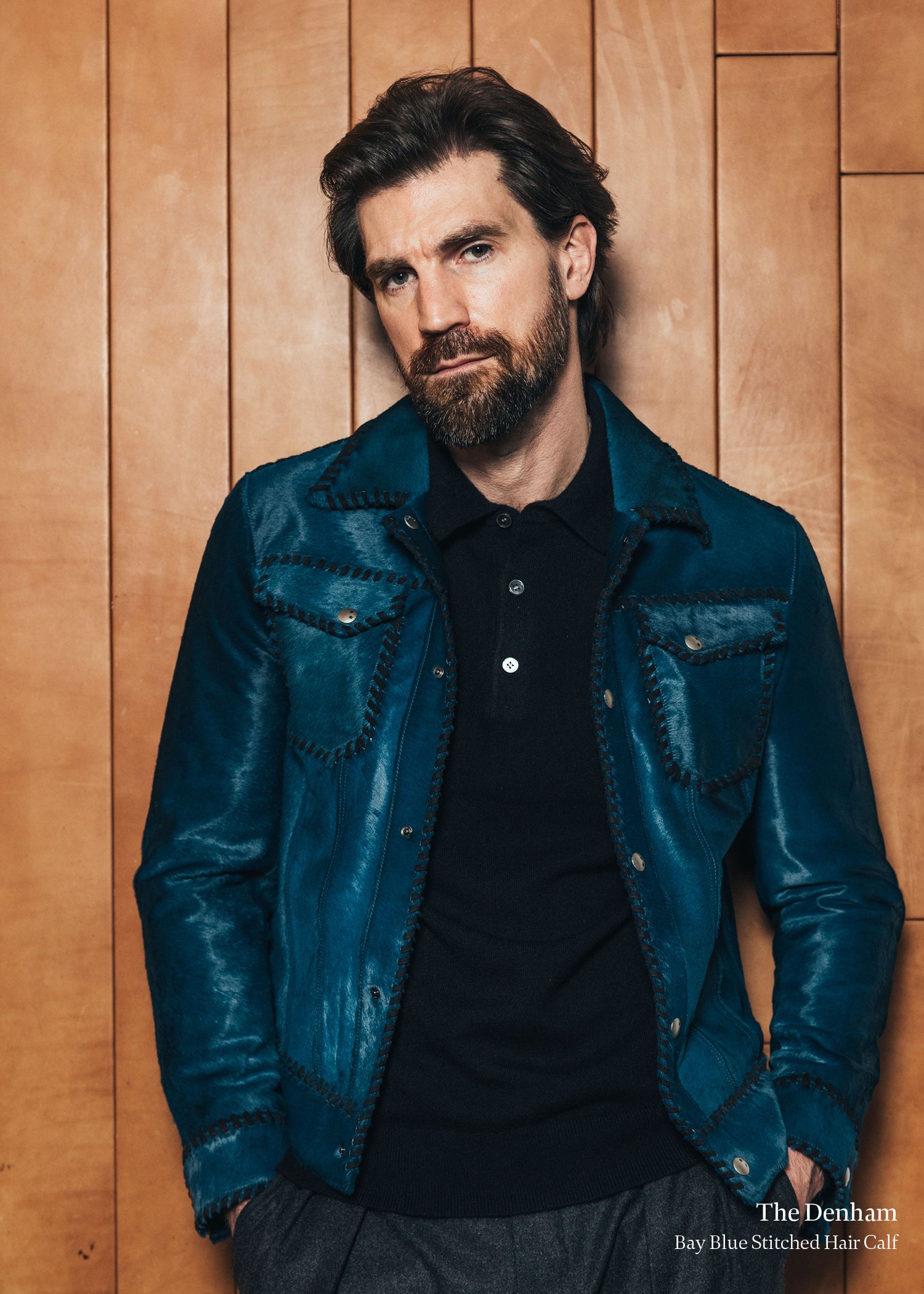Man wearing a blue denim jacket against a wooden paneled wall