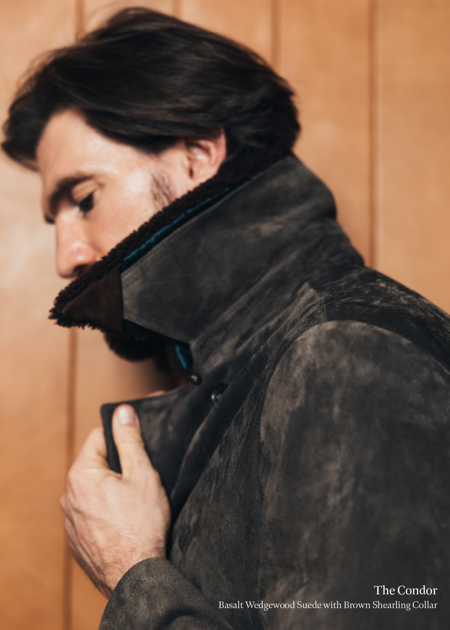 Man wearing a dark brown suede jacket with a shearling collar against a wooden background