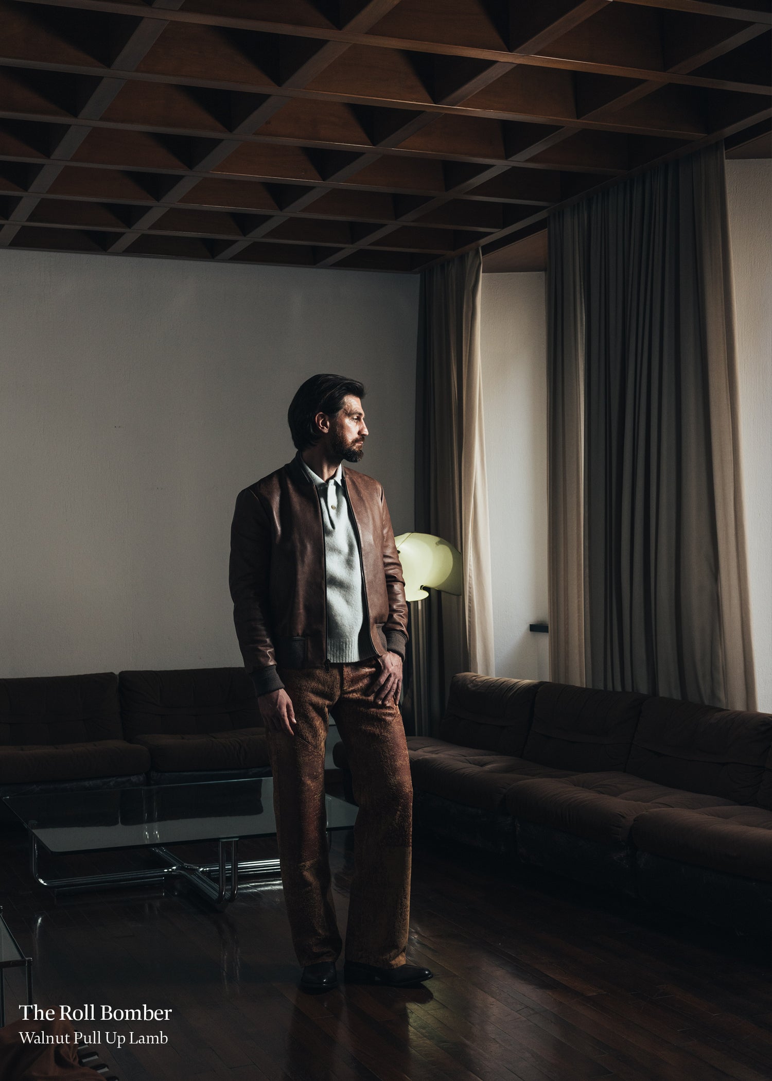 Man in a brown suit standing in a dimly lit room with a modern interior.