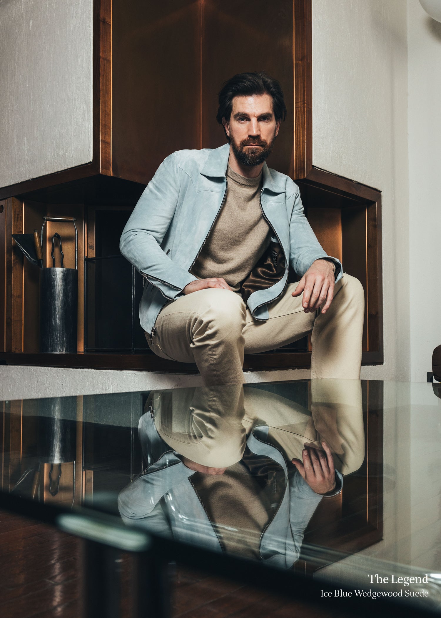Man sitting on a reflective surface with a stylish outfit, surrounded by modern interior design.
