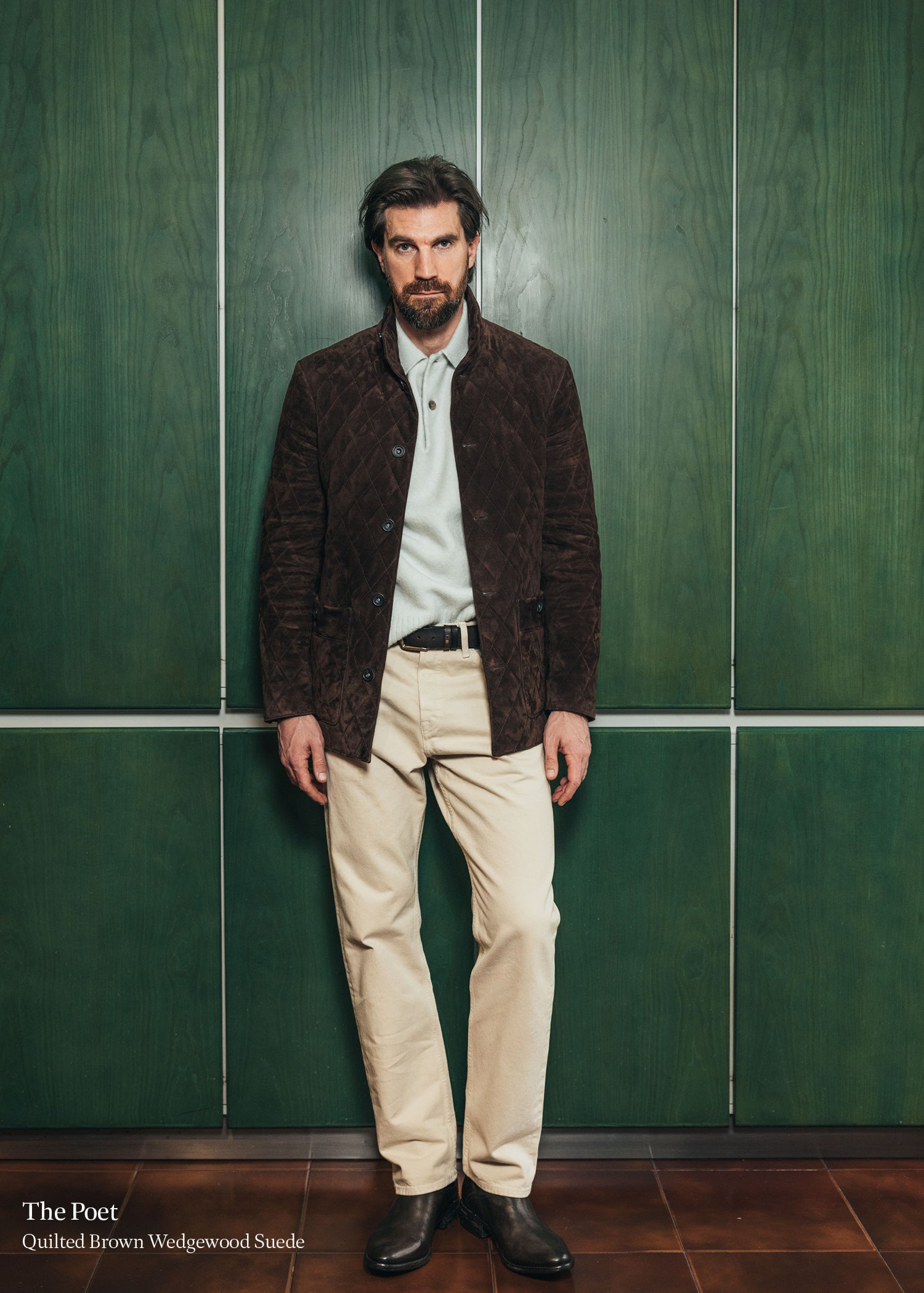 Man wearing a brown quilted jacket against a green tiled wall.