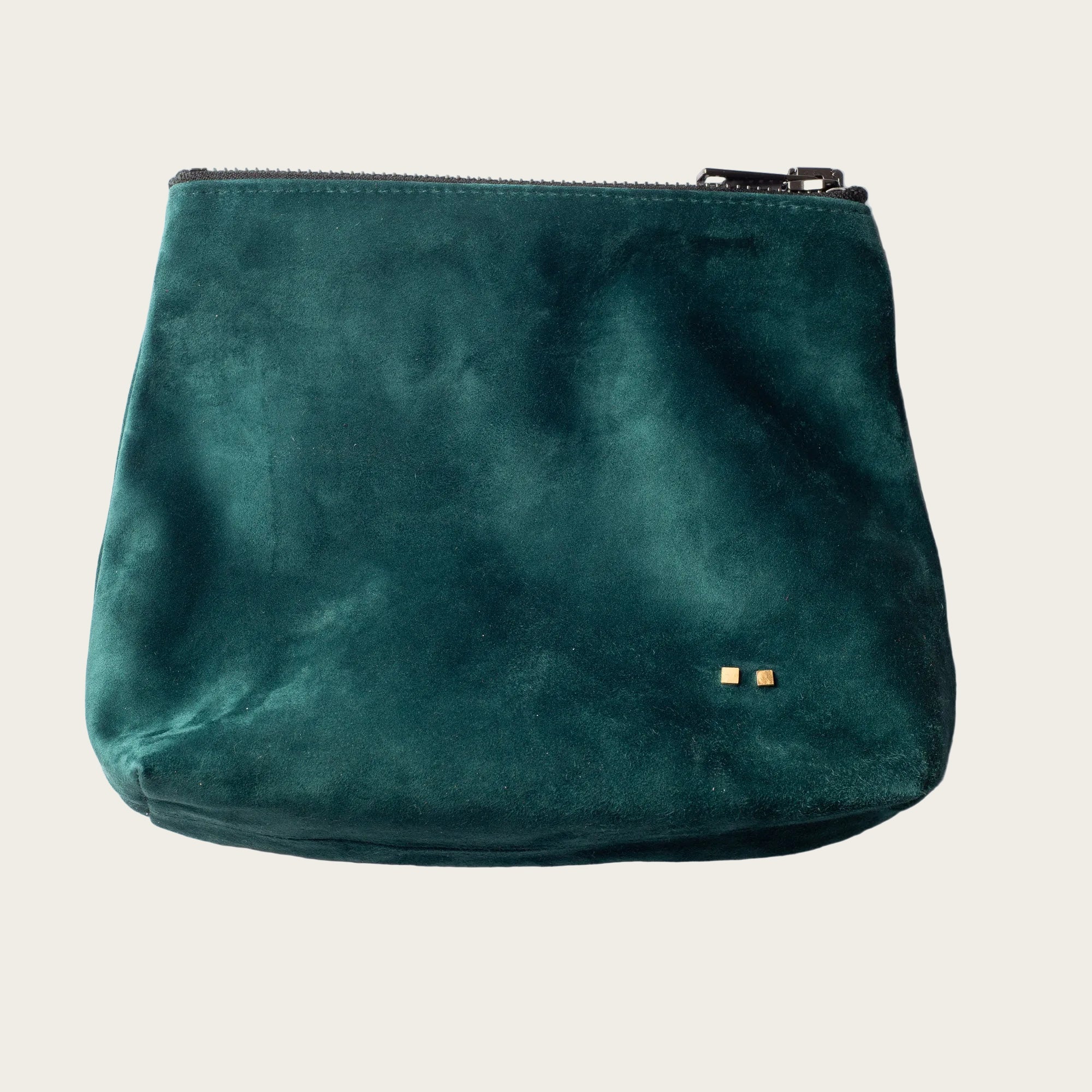 Green suede pouch with gold zipper on a beige background