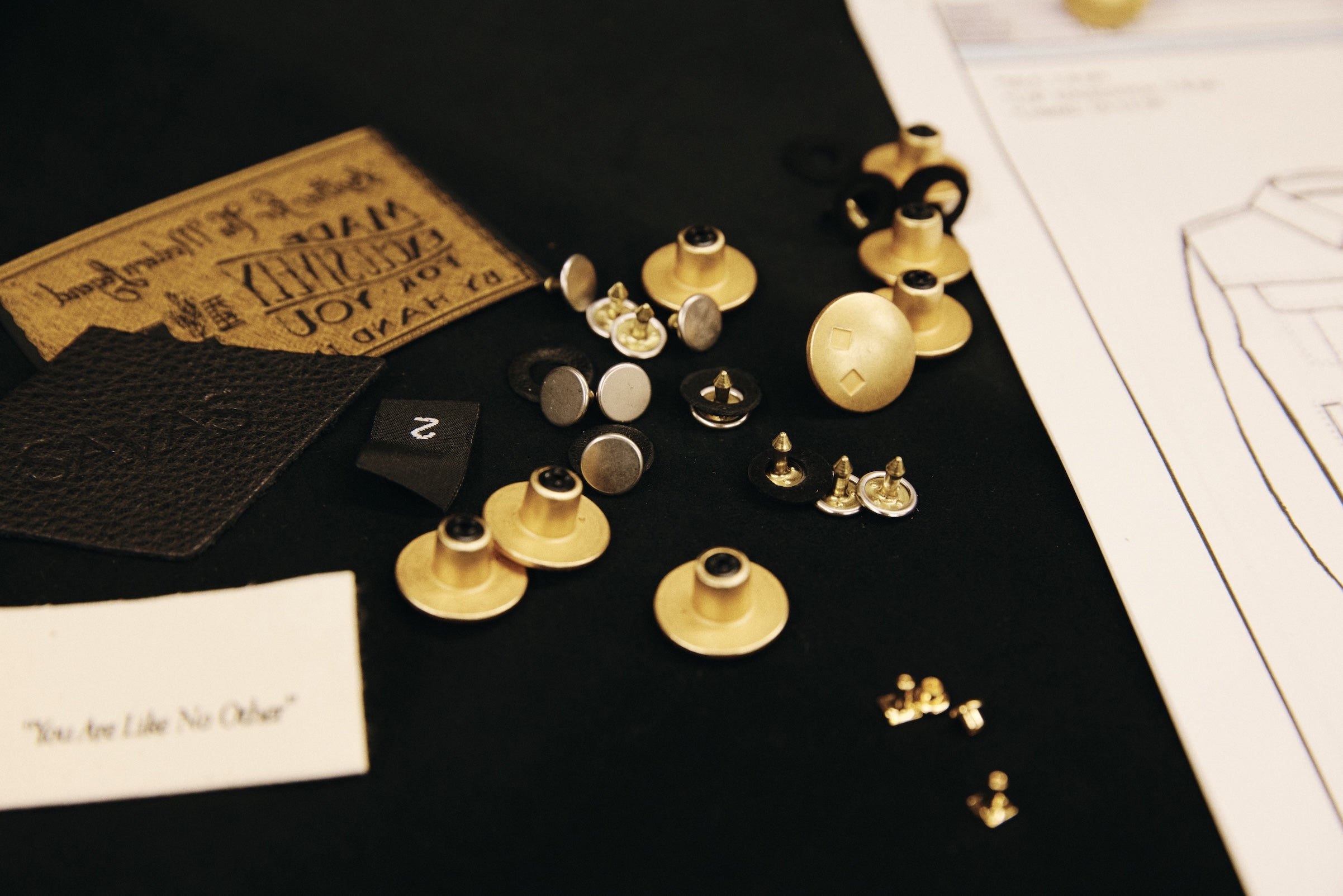 Close-up of Savas branded rivets on dark fabric swatch and sketch