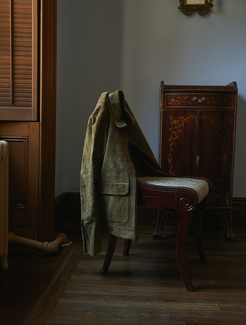 Image of an olive suede Savas jacket draped on a chair.